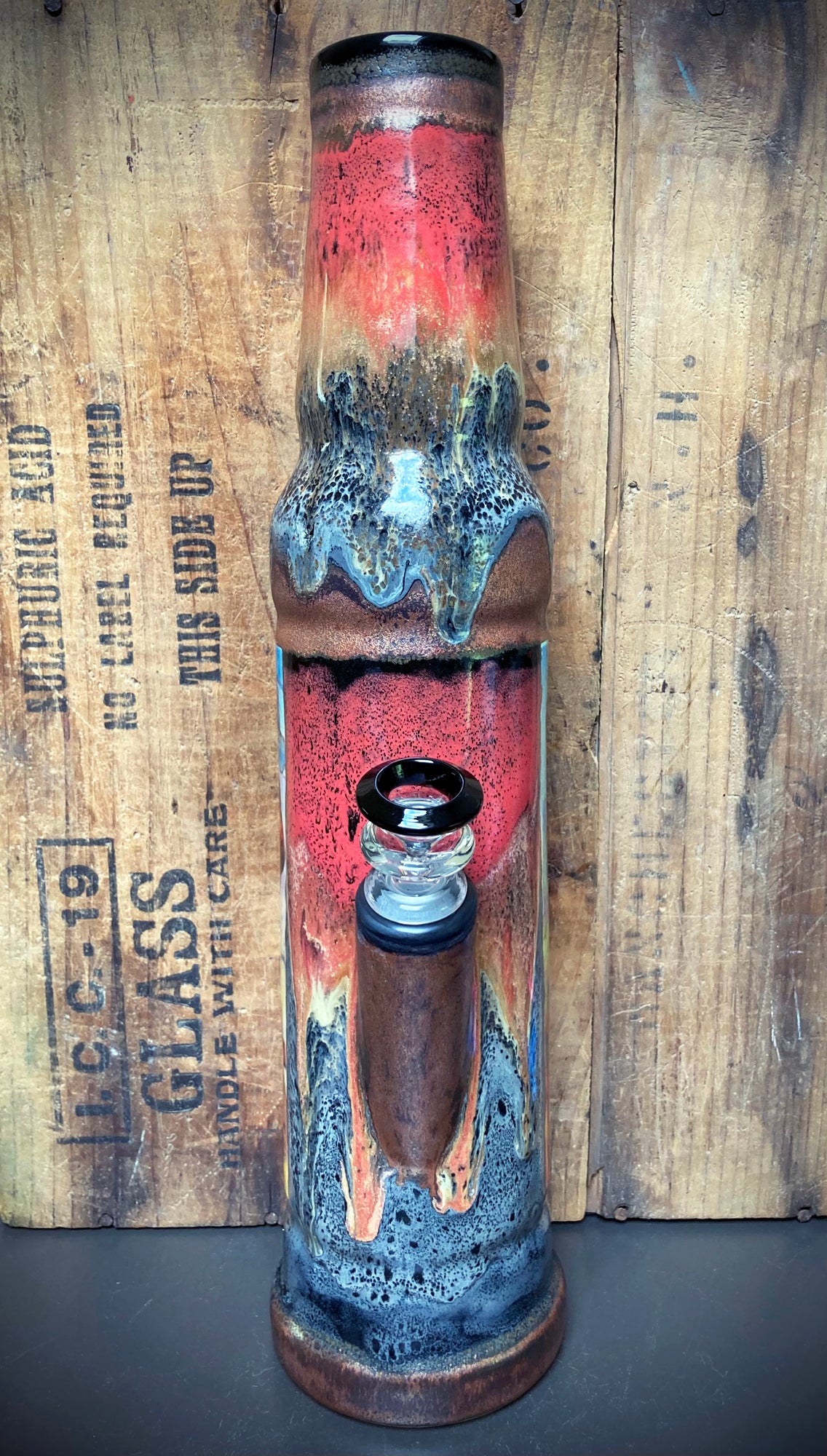 Bright red, orange, green, and blue glazes highlight dinosaur jungle art on ceramic bong.