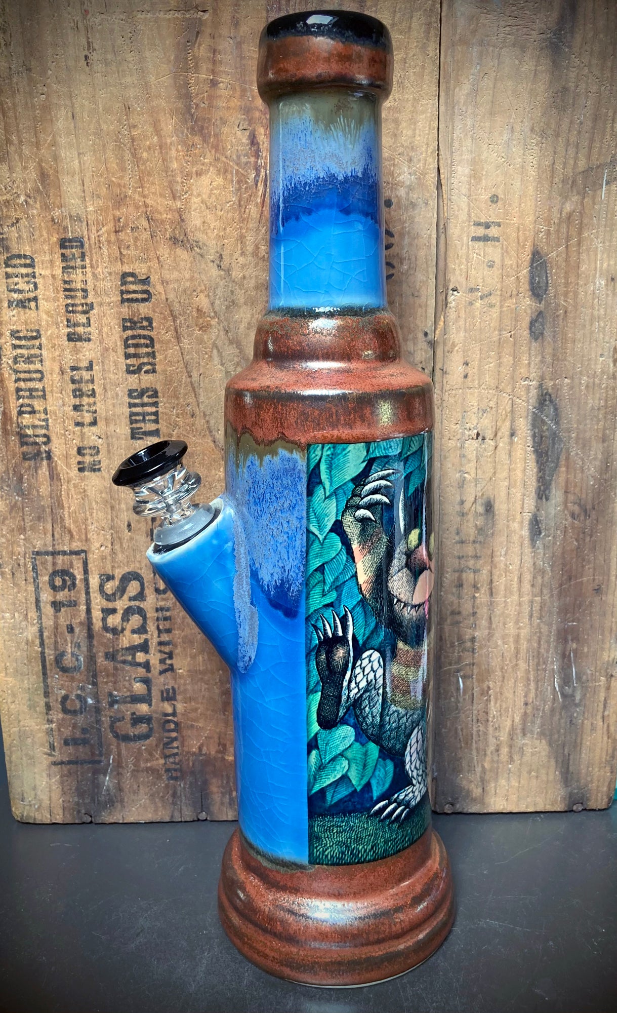 Side view showing blue and rust drip glaze and vivid monster scene