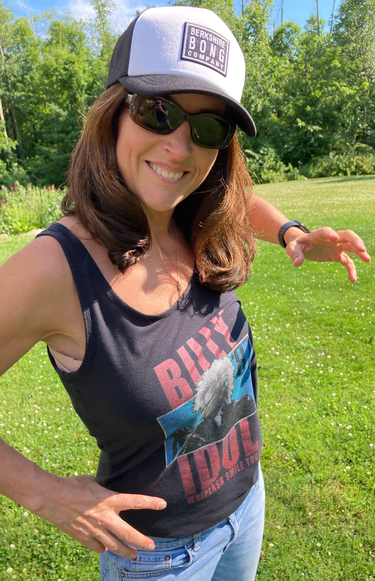 Woman wearing Berkshire Bong Company Trucker Hat and a black tank top, smiling outdoors in a grassy field