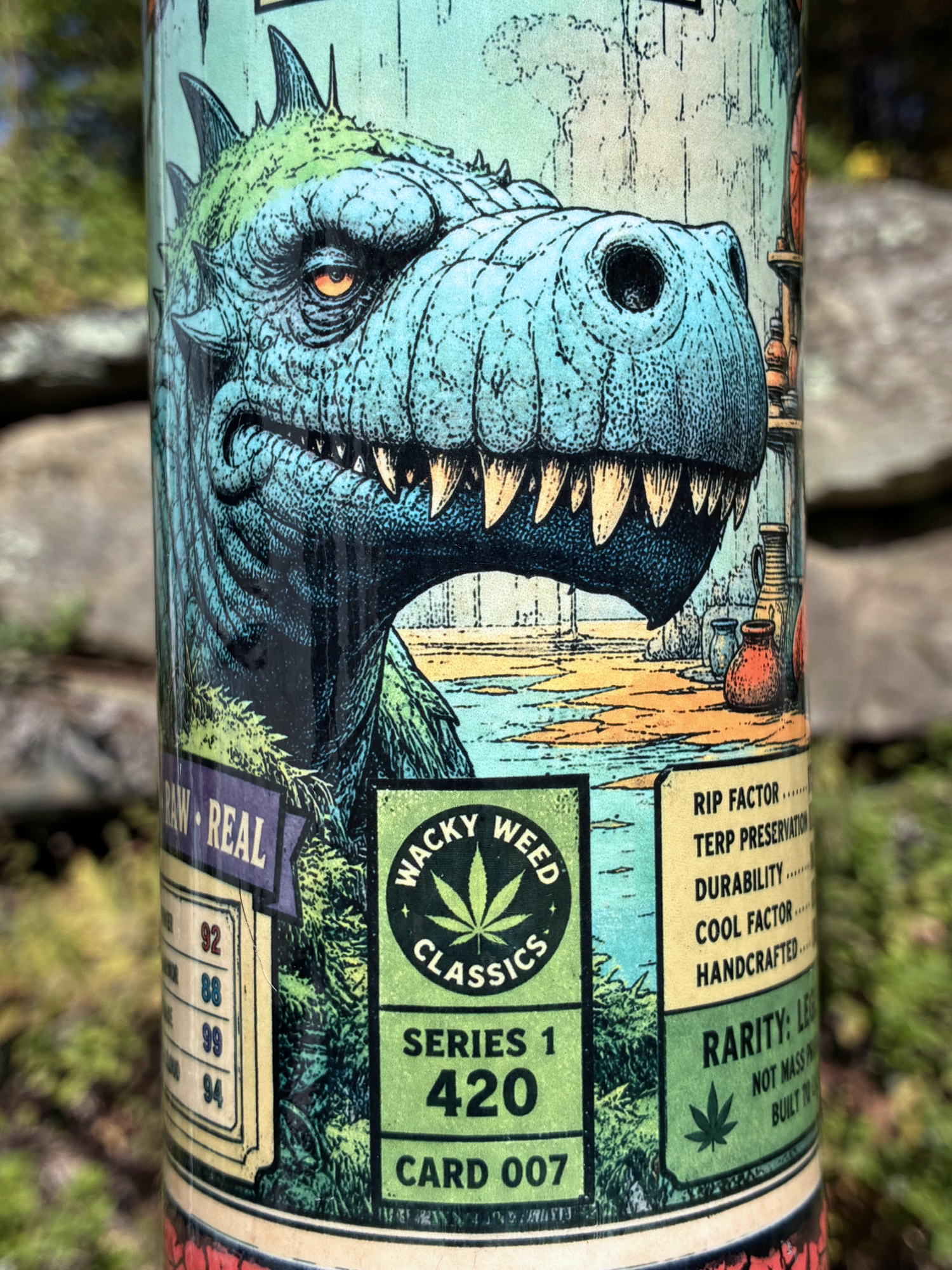 Monster Rips handmade ceramic bong featuring blue-green dinosaur collector-card artwork, deep red crackle glaze and glossy black accents.