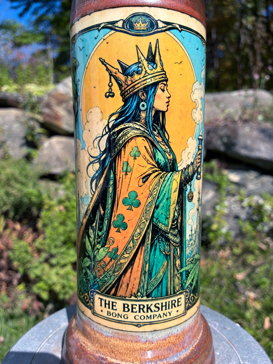 Queen of Clubs handmade ceramic bong featuring crowned queen playing-card artwork, softly flowing blue and lavender glaze, and copper-brown accents.
