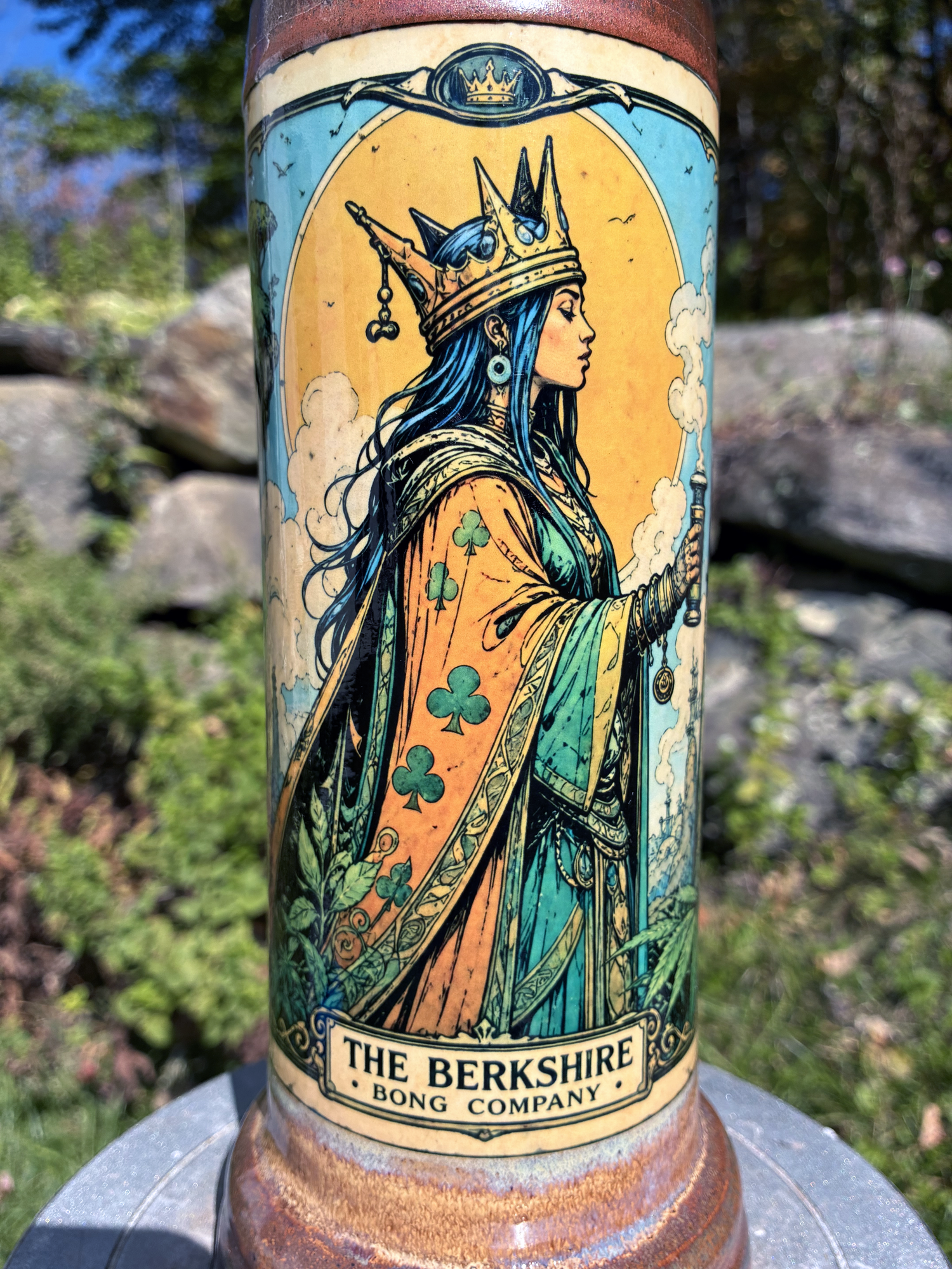 Queen of Clubs handmade ceramic bong featuring crowned queen playing-card artwork, softly flowing blue and lavender glaze, and copper-brown accents.